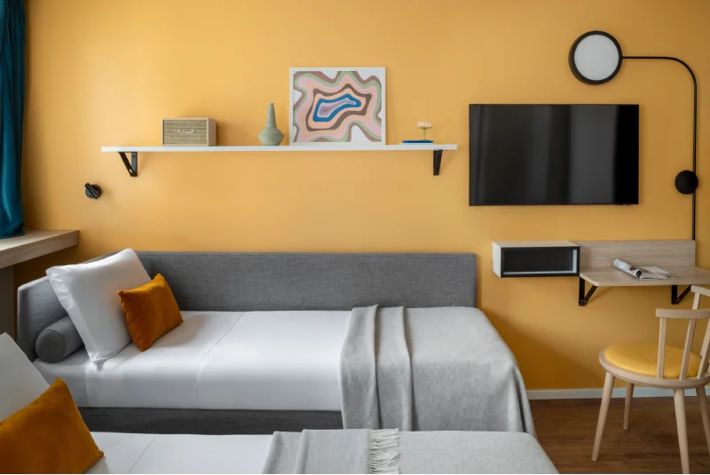 Living area with sofa bed, yellow wall, TV and desk for practical and relaxing stays - Aparthotel Colombo, BZAR hotels in Rome