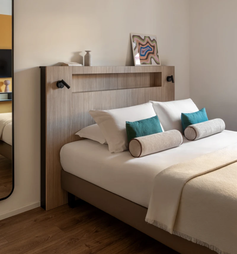 Modern double room with wood headboard, turquoise cushions and full-length mirror - Aparthotel Colombo, BZAR hotels in Rome