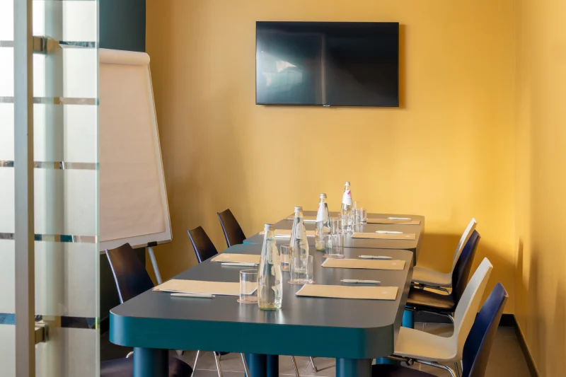 Modern meeting room with blue table, flip chart, wall TV and professional meeting setup - Aparthotel Colombo, BZAR hotels in Rome
