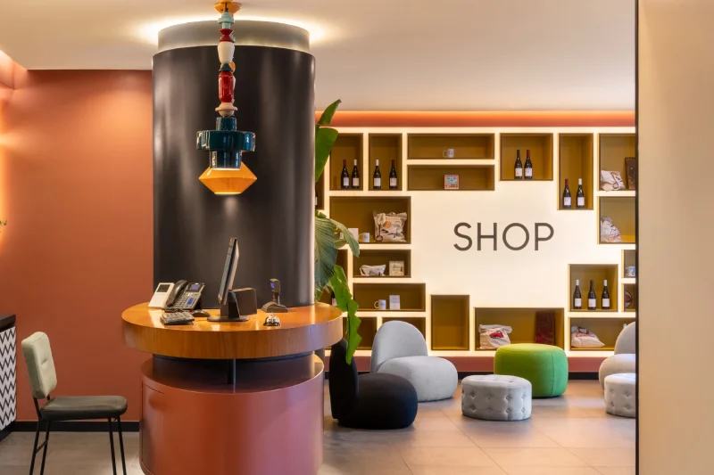 Reception di design con banco rotondo, shop interno, scaffali illuminati e lounge colorata - Aparthotel Colombo, BZAR hotels a Roma