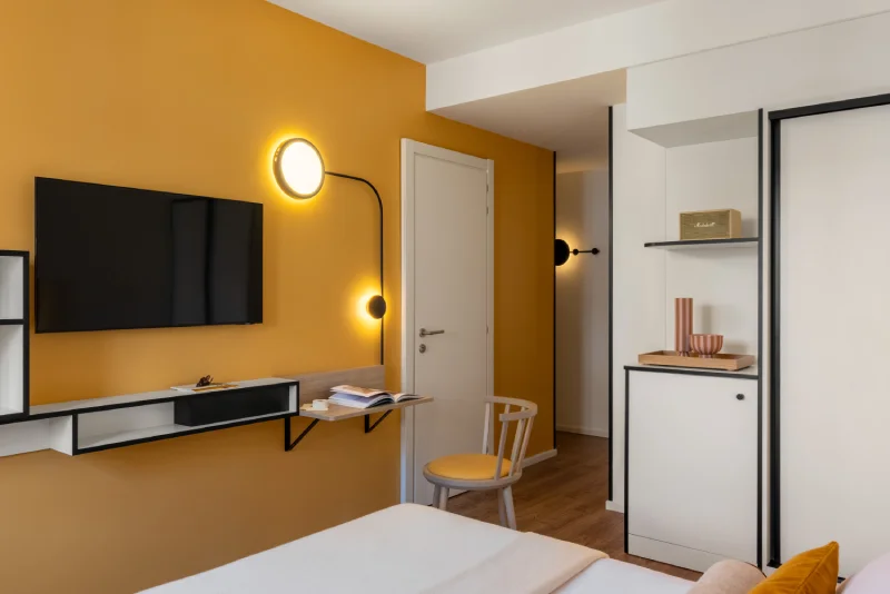 Standard room with mustard wall, floating TV, compact desk and modern wardrobe - Aparthotel Colombo, BZAR hotels in Rome