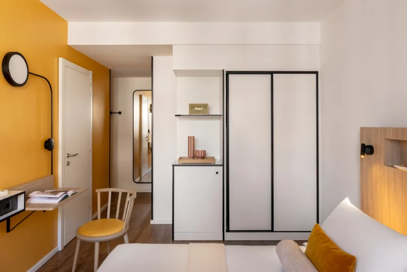 Standard room with white wardrobe, mustard wall, matching chair and contemporary details - Aparthotel Colombo, BZAR hotels in Rome