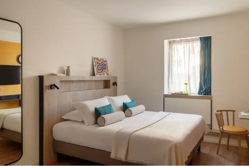 Superior room with double bed, turquoise cushions, tall mirror and bright window - Aparthotel Colombo, BZAR hotels in Rome