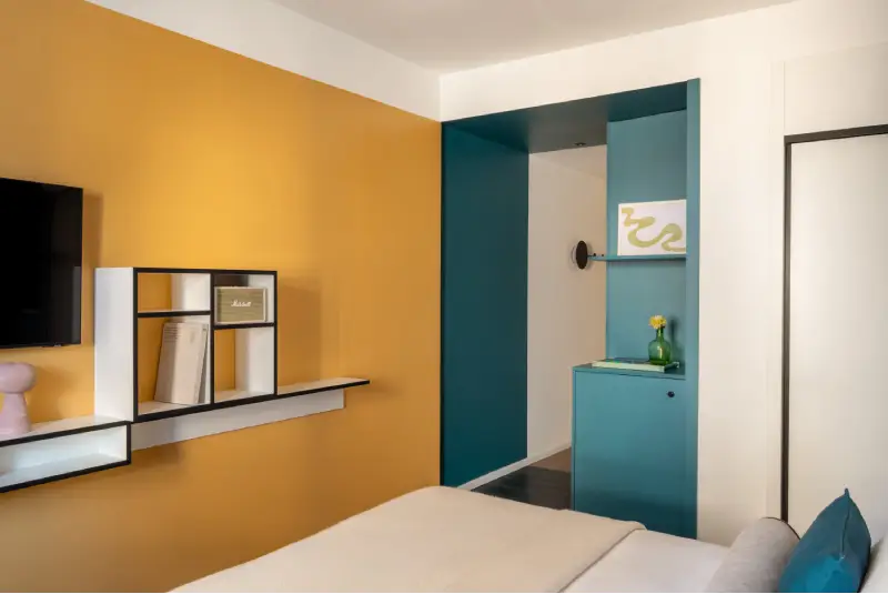 Superior room with mustard wall, turquoise cabinet, modern shelves and double bed - Aparthotel Colombo, BZAR hotels in Rome